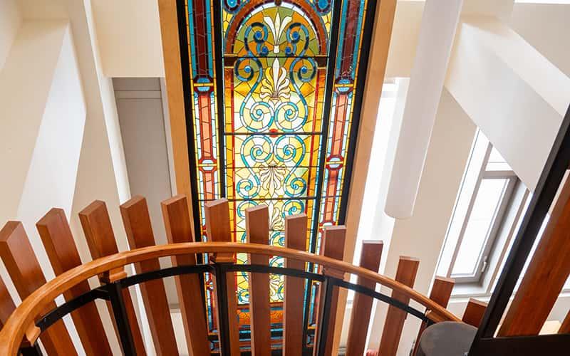 a view of a stained glass window in Buley Library, with stairway bannister in the foreground