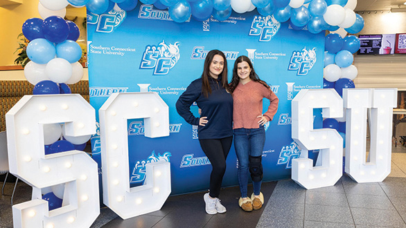 Two accepted Southern Connecticut students with the Southern sign in lights behind them