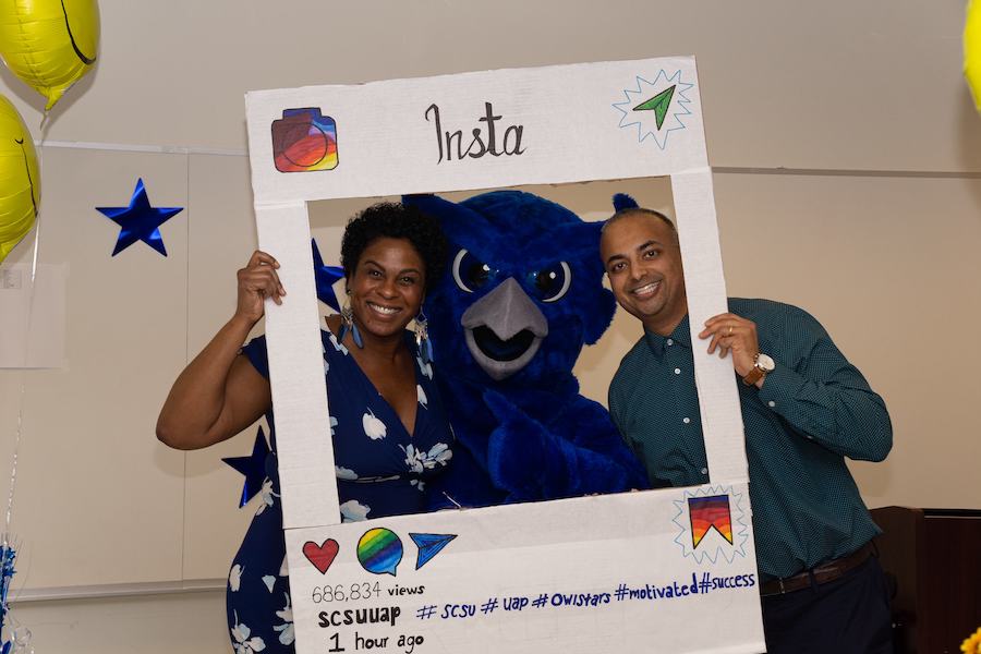 Two UAP staff and the SCSU owls mascot inside an Instagram picture frame cutout