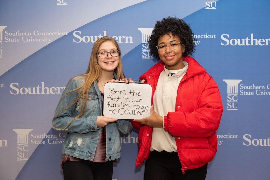 Two girls holding a sign together, about being first generation grads