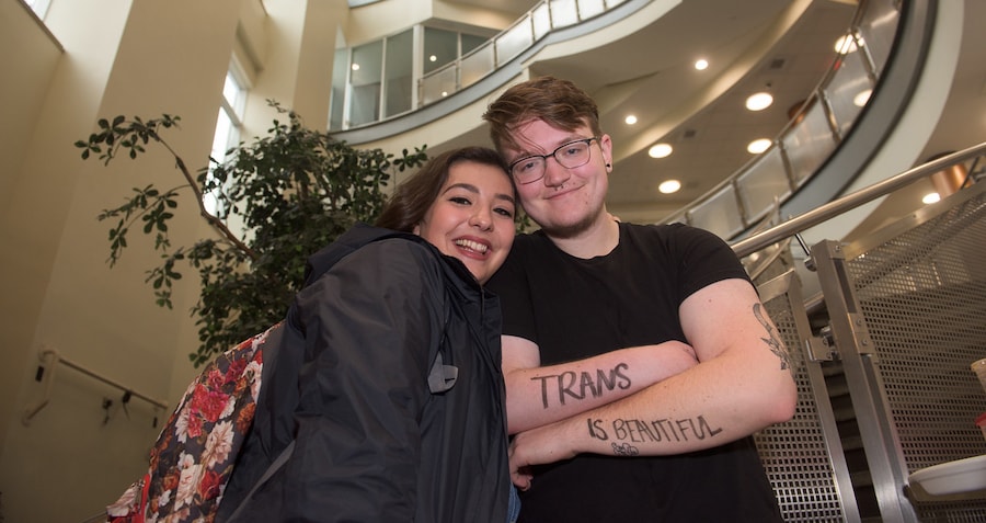 Two students inside the SCSU student center, with one student that has a tattoo of 'Trans in beautiful'