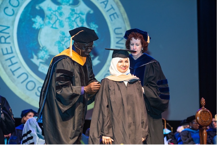 A student in cap and gown at her graduation ceremony being congratulated
