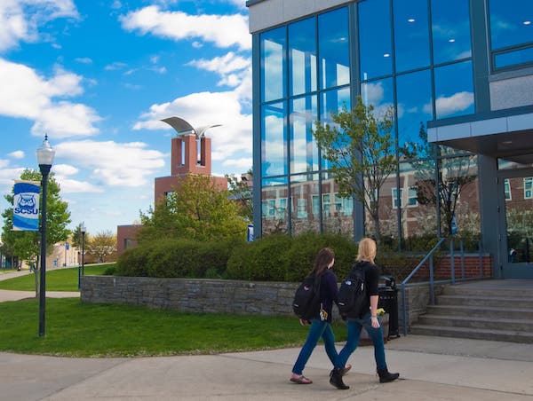"Academic building and two students walking towards an academic building"