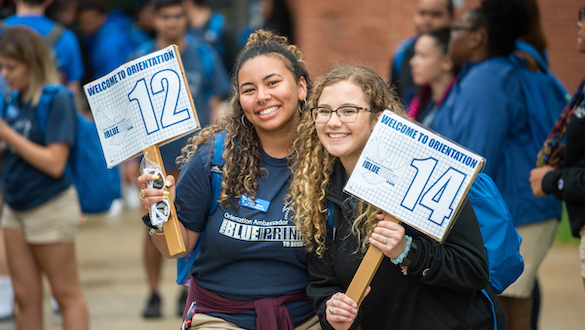 Two smiling students holding orientation signs