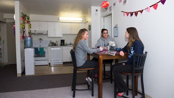 Three women sitting around a dining table at a dorm room