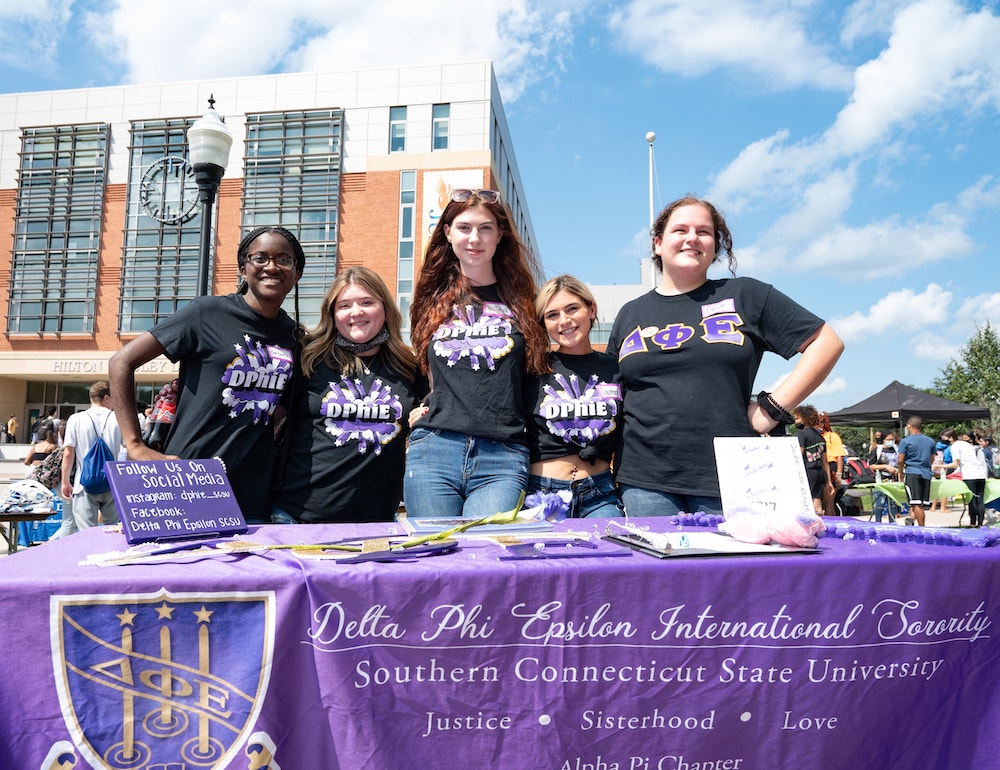 A group of female sorority students outside an academic quad in a club fair table, representing their sorority