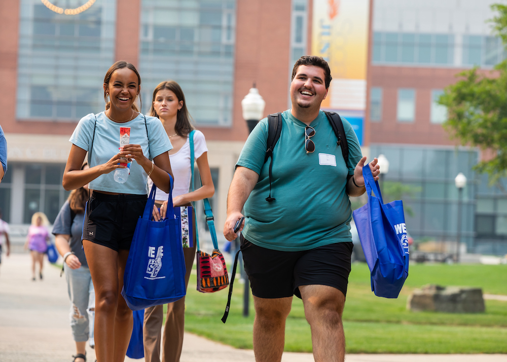 Three students in academic quad and other students in the background