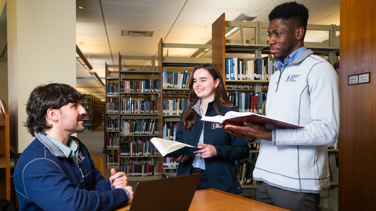 Three students reviewing informaton on a computer and books