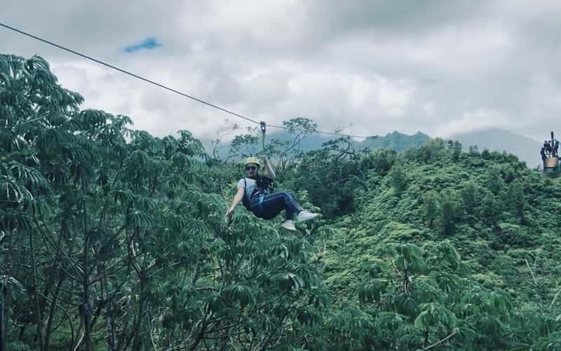 a student ziplines against a background of trees and vegetation