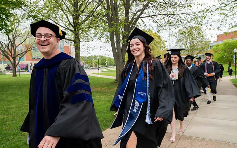 students and faculty in caps and gowns walk across the SCSU campus
