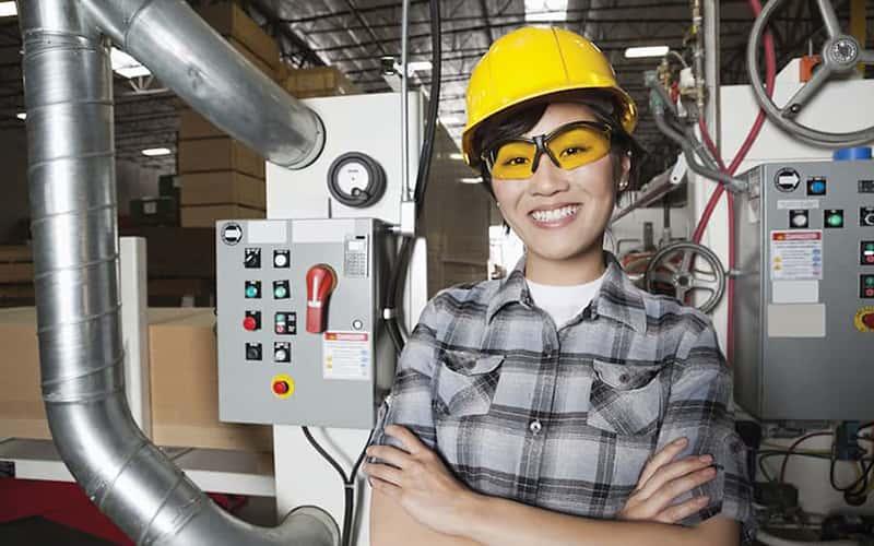 a person in a yellow hard hat stands in front of machinery and industrial equipment