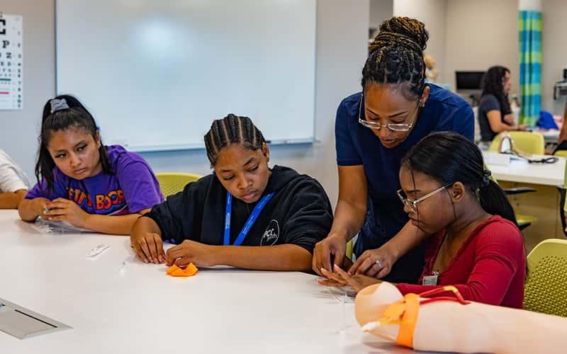 a nursing professor works closely at a table with three young students