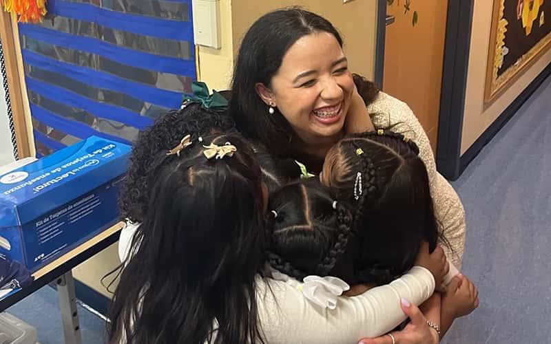 Student teacher Hilbania Papazahariou hugs four of her young pupils