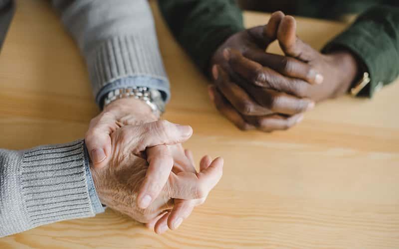 two pairs of clasped hands rest on a table