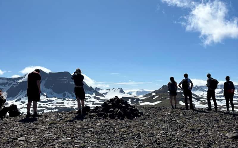 six people stand atop a mountain looking out at the view