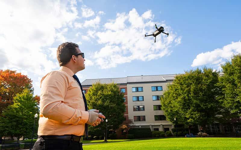 a student flies a drone in front of a campus building