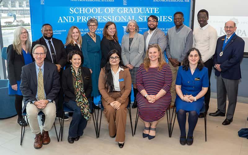 Group of faculty, staff, and graduate students pose for a photo in front of a Southern Connecticut State University School of Graduate and Professional Studies backdrop during the installation ceremony of Phi Kappa Phi Chapter #365.
