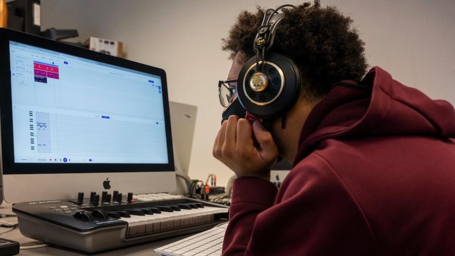 "A student with headphones and music keyboard editing music with software"