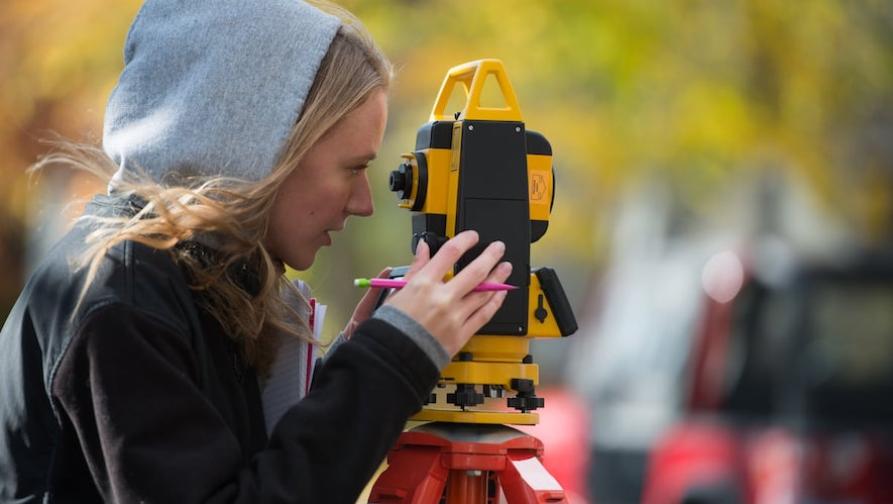 A student surveying an area using surveying tools