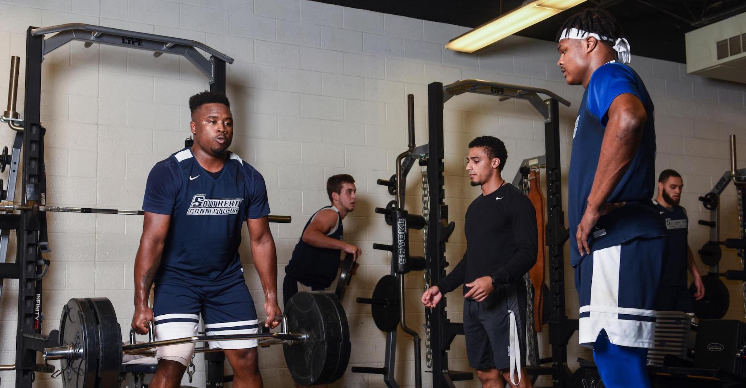 Man lifting weights and two other men watches