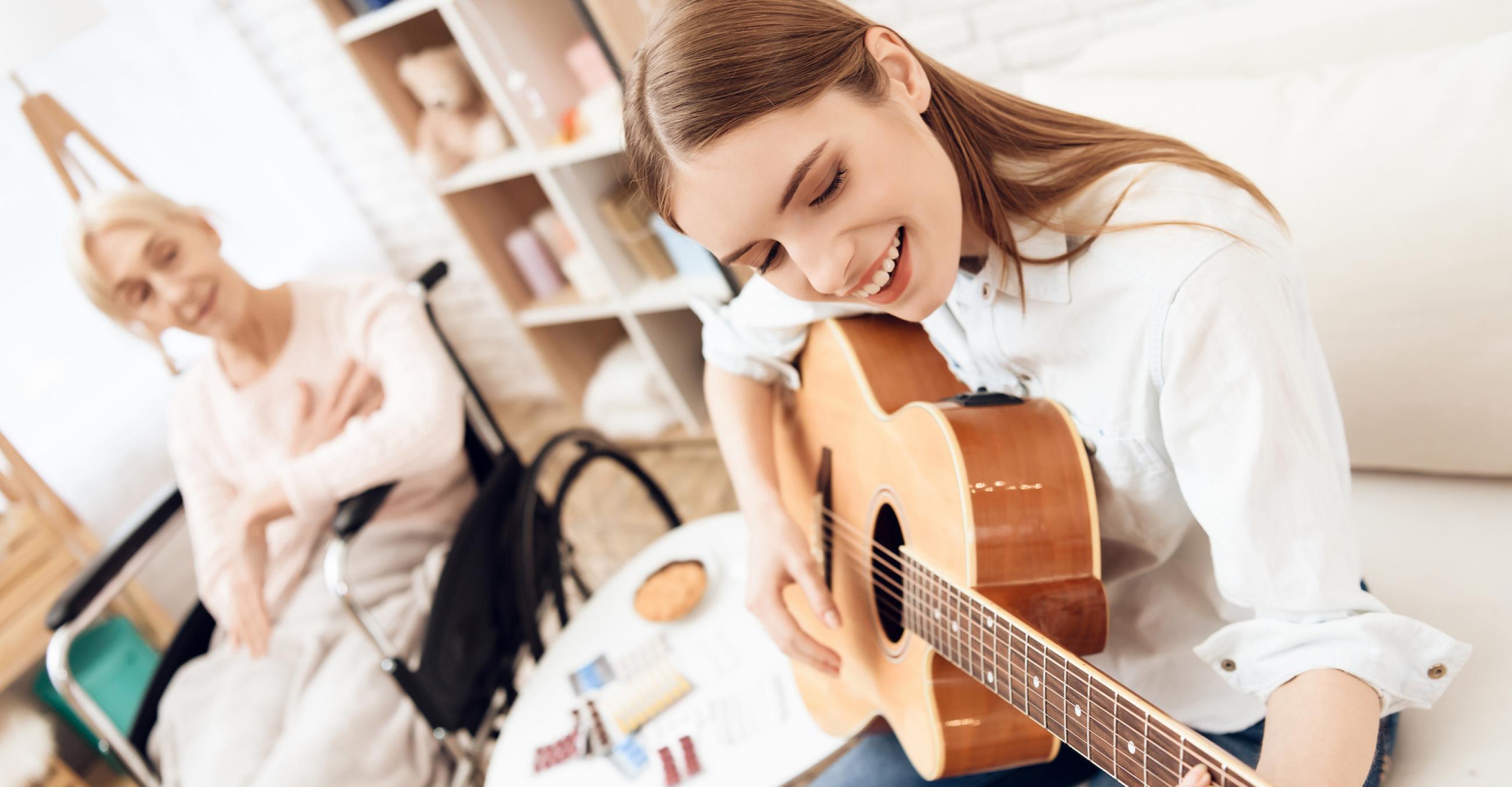 "A student playing guitar and an instructor listening"