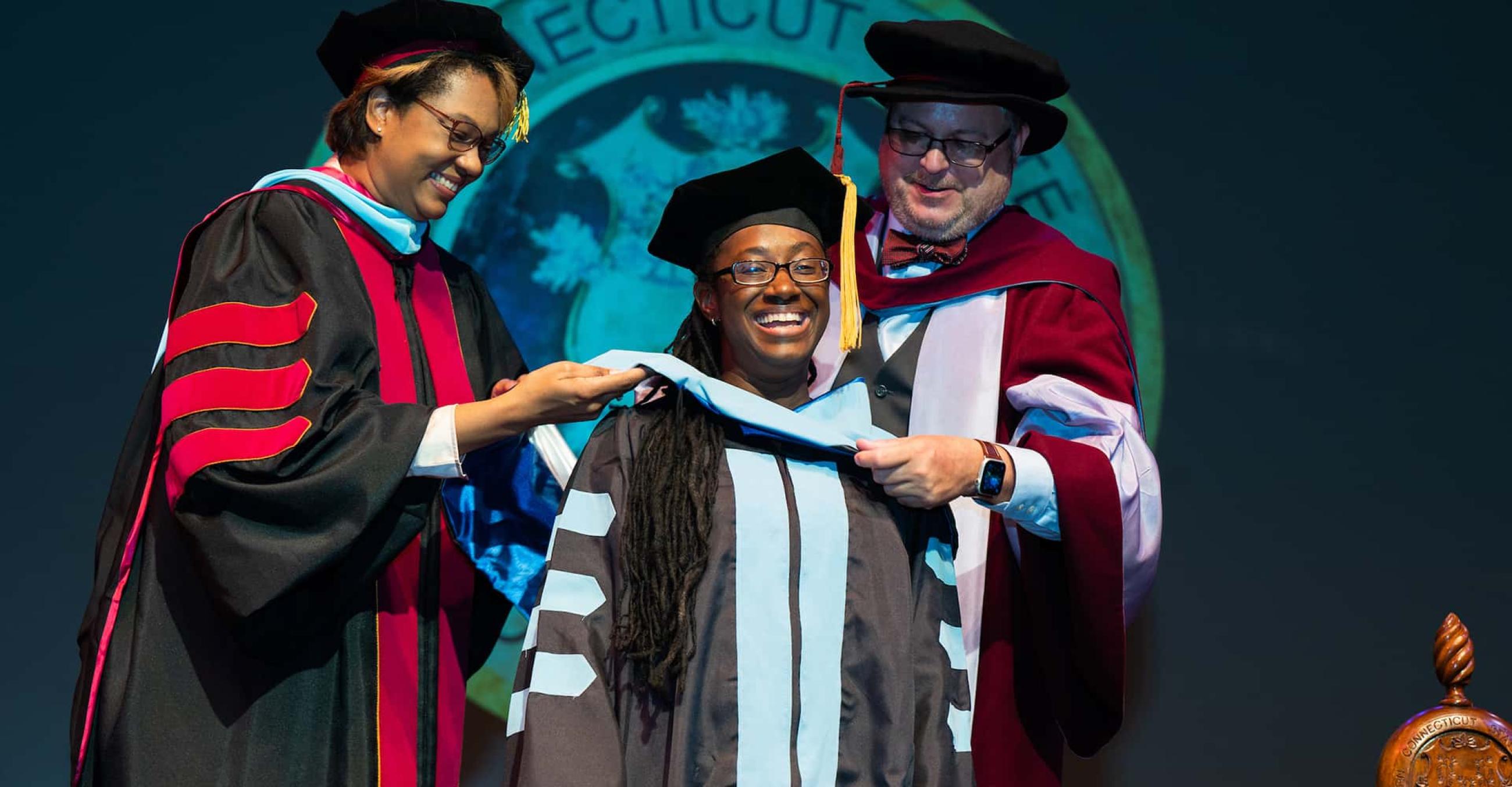 a graduate student receives her hood from two faculty members at Graduate Commencement