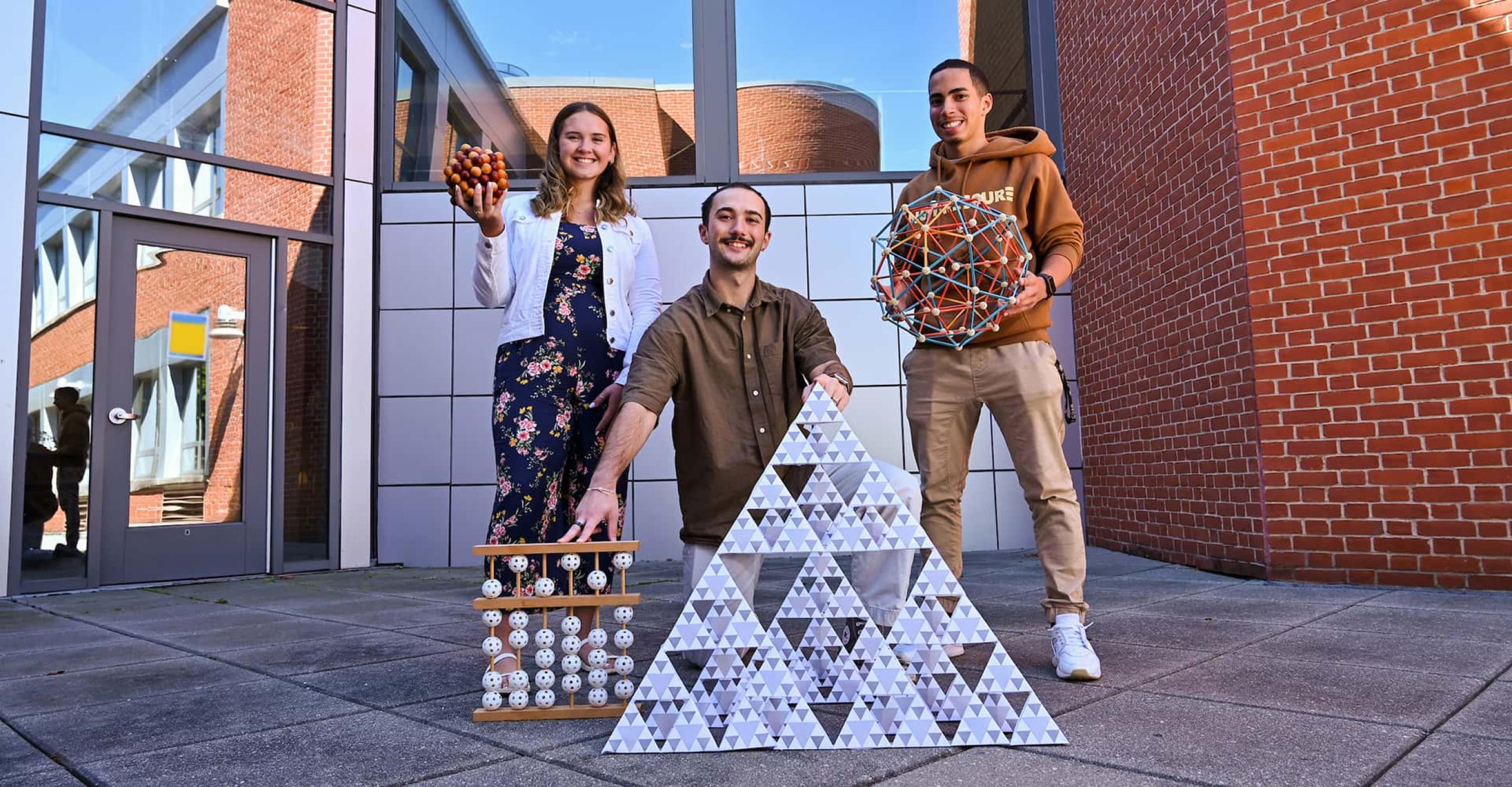 three students pose with objects related to math and science
