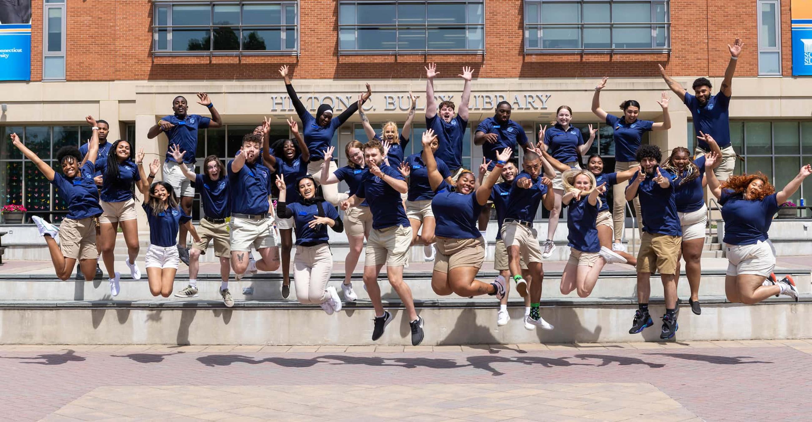 a group of students leap into the air in front of the library