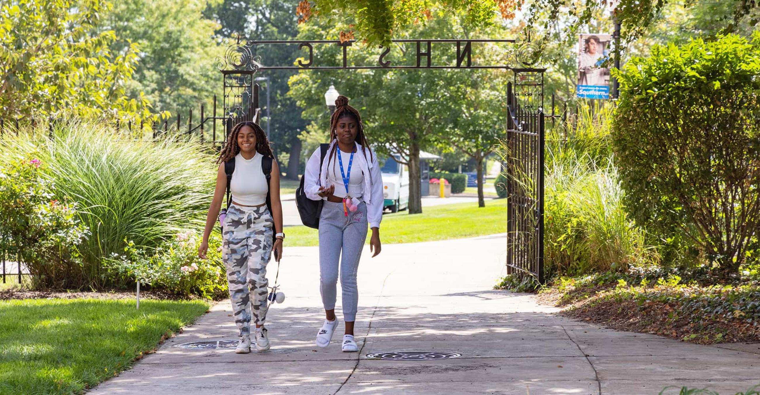 two students walk through Founders Gate on campus