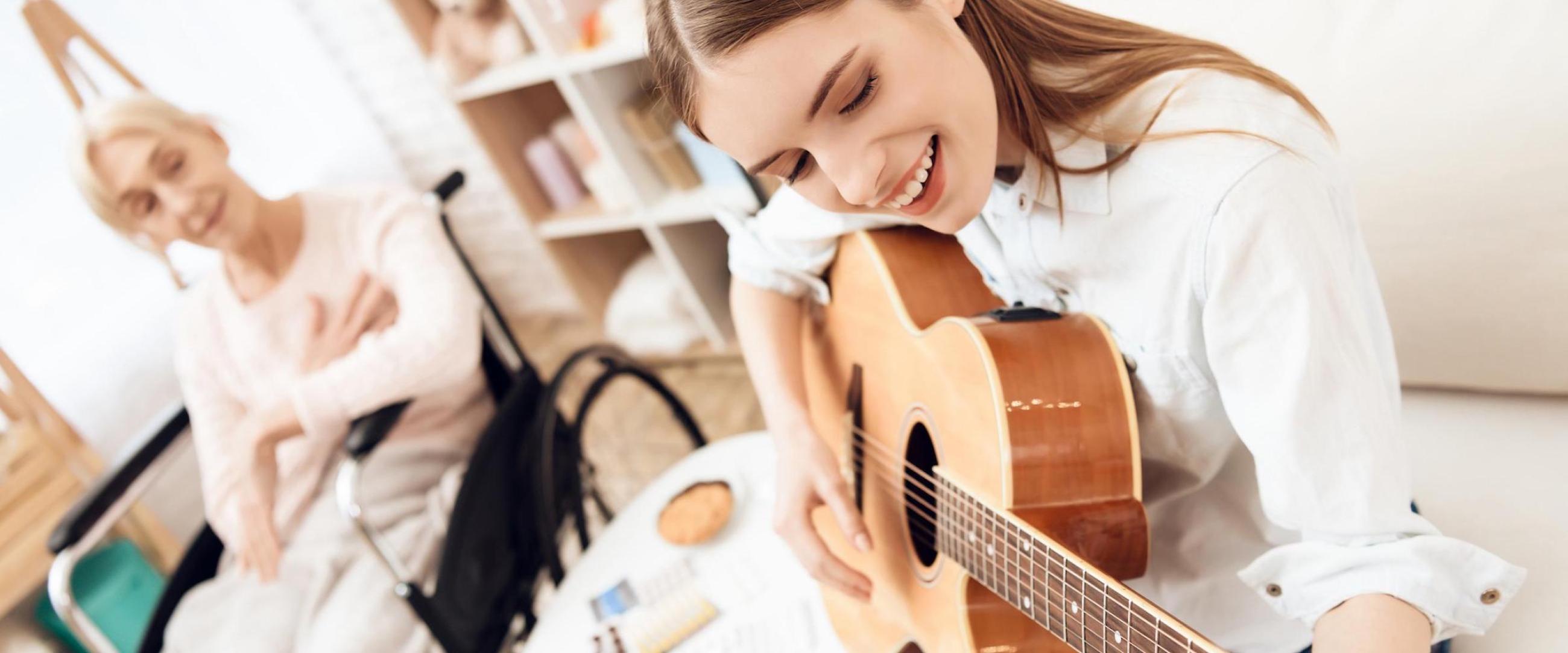 Woman playing guitar with an elderly woman behind listening