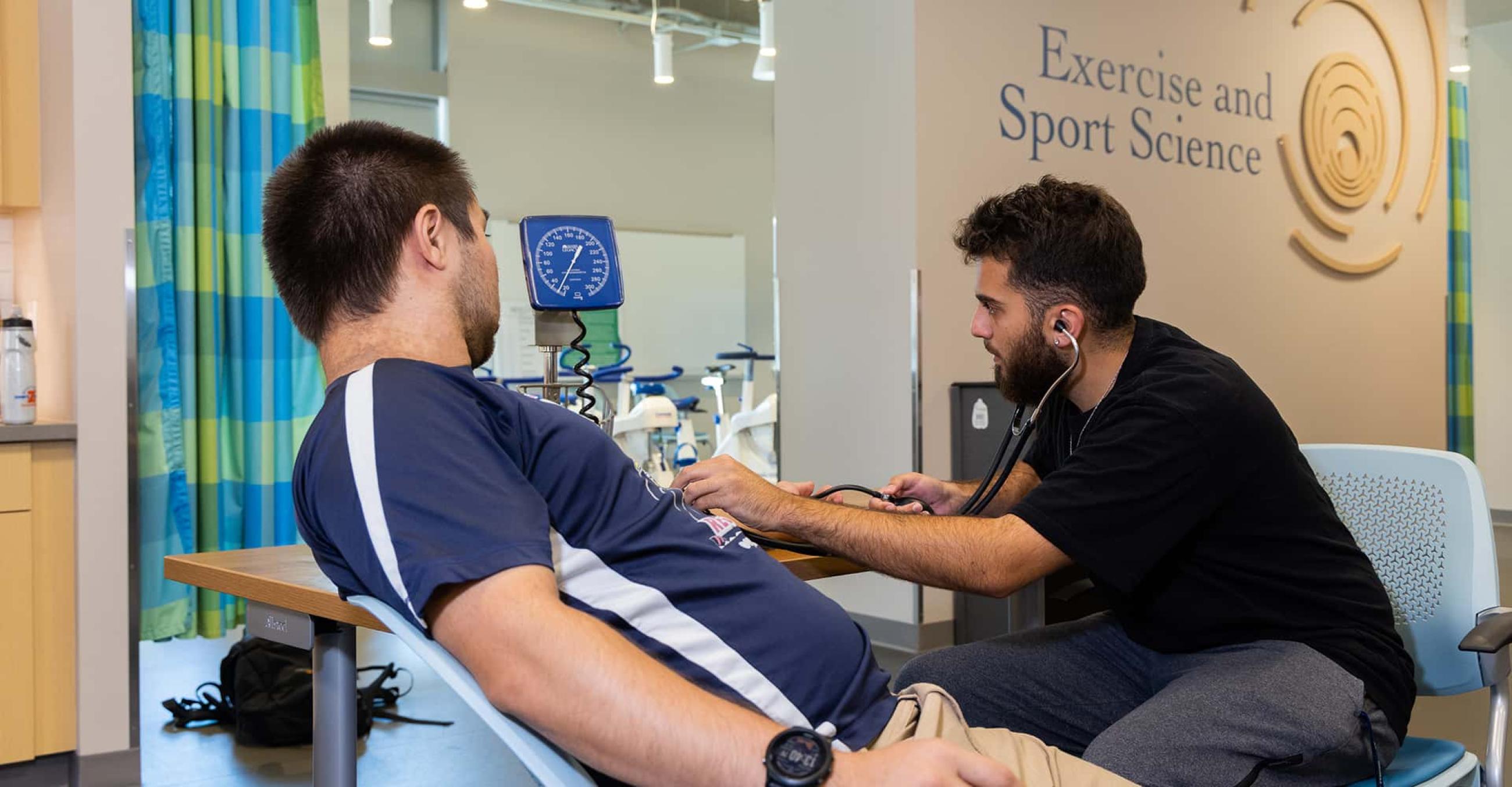 a student holds a stethoscope to another student's chest as if to listen to his heart