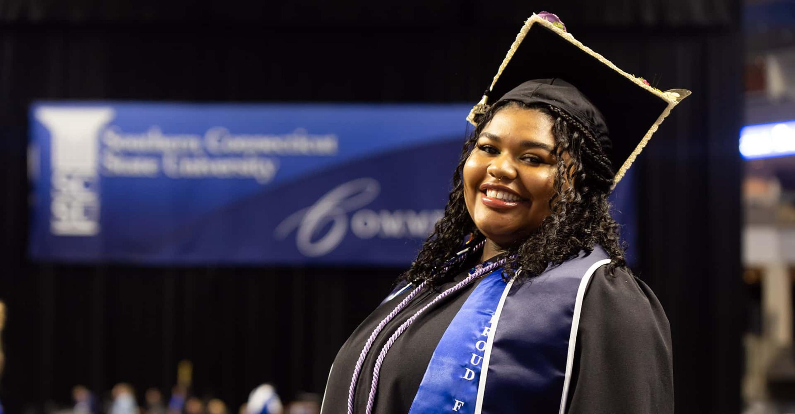 a student in cap and gown smiles at the camera