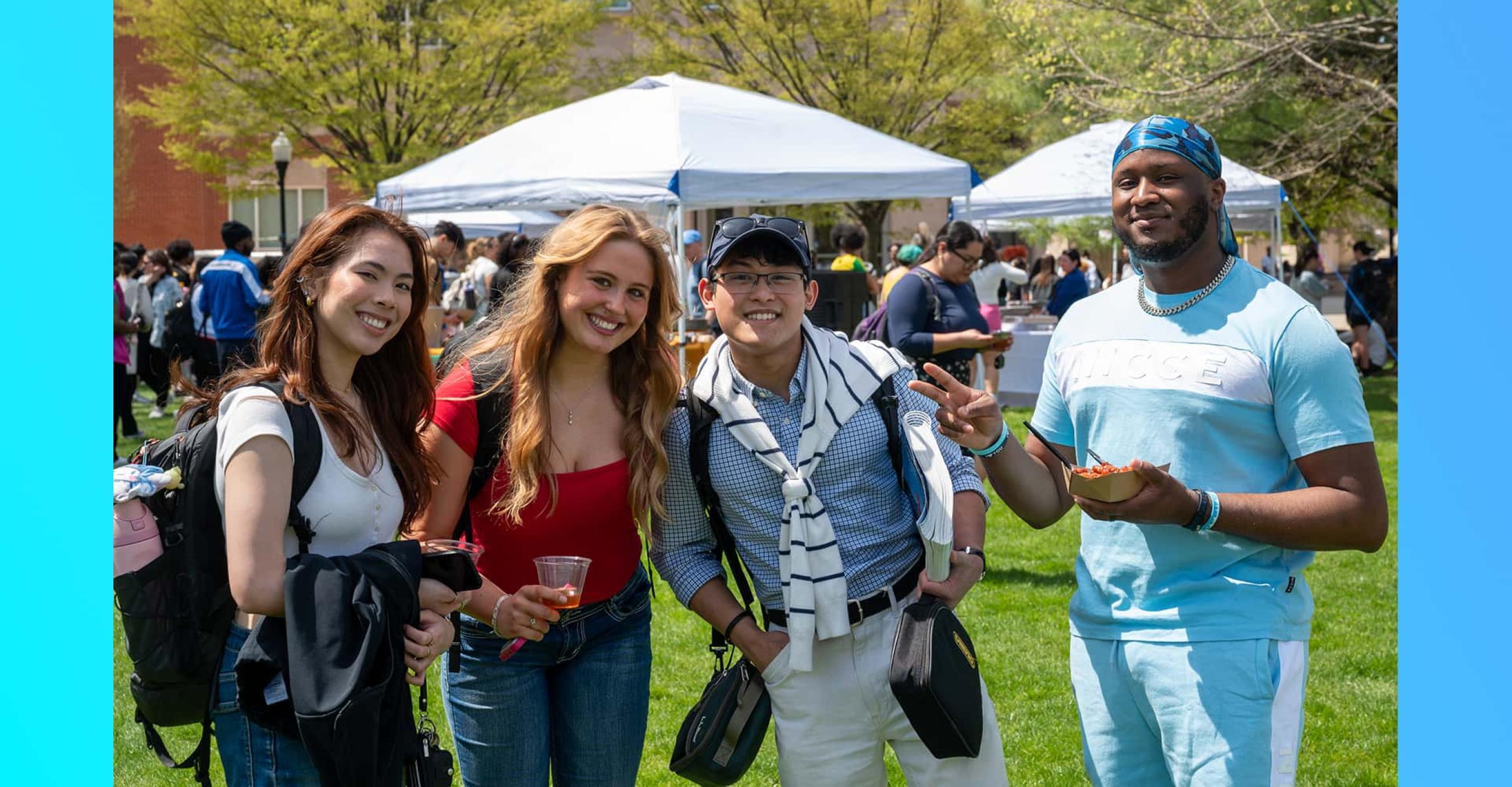 a group of four smiling students outdoors on the campus quad