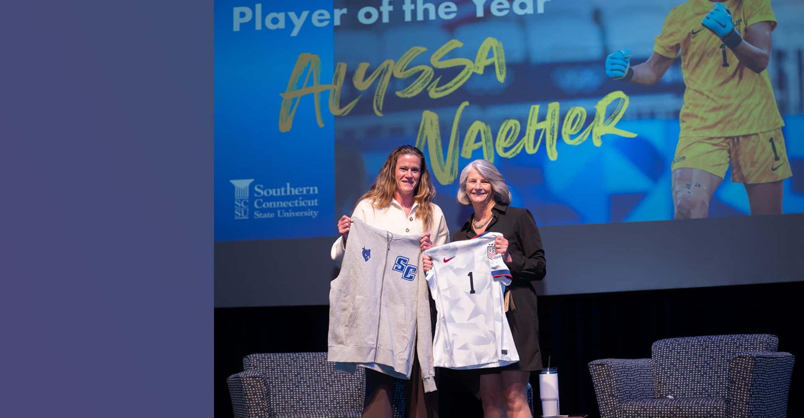 Alyssa Naeher and SCSU Interim President Sandy Bulmer hold up SCSU shirts on the Lyman stage