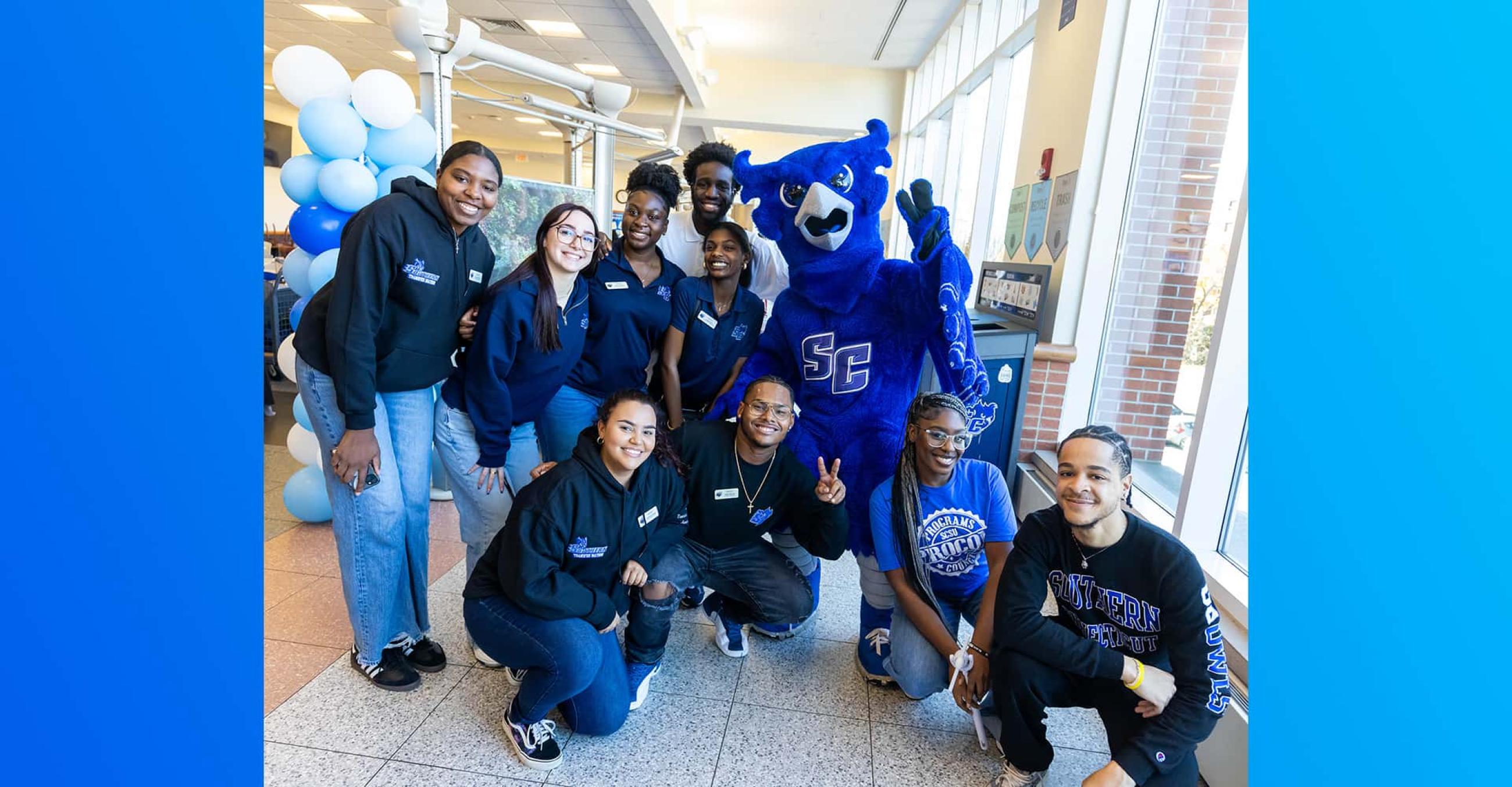 a group of students stand with Otus the Owl mascot