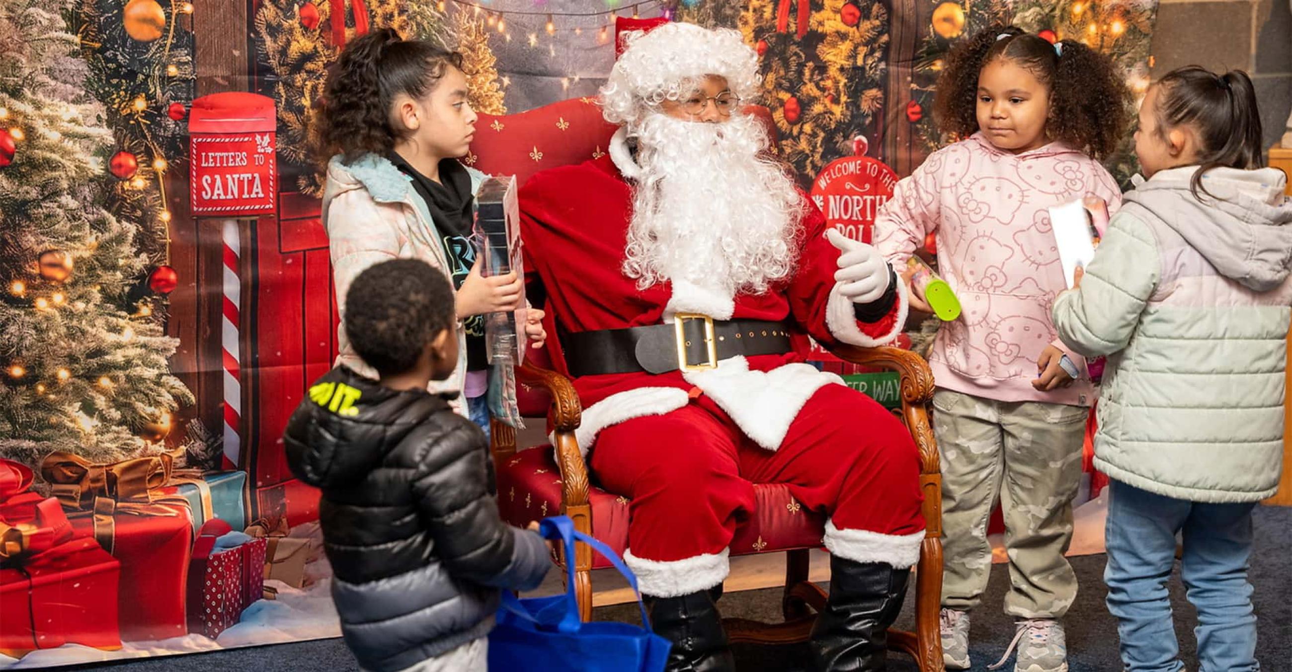 a seated Santa Claus talks with four young children