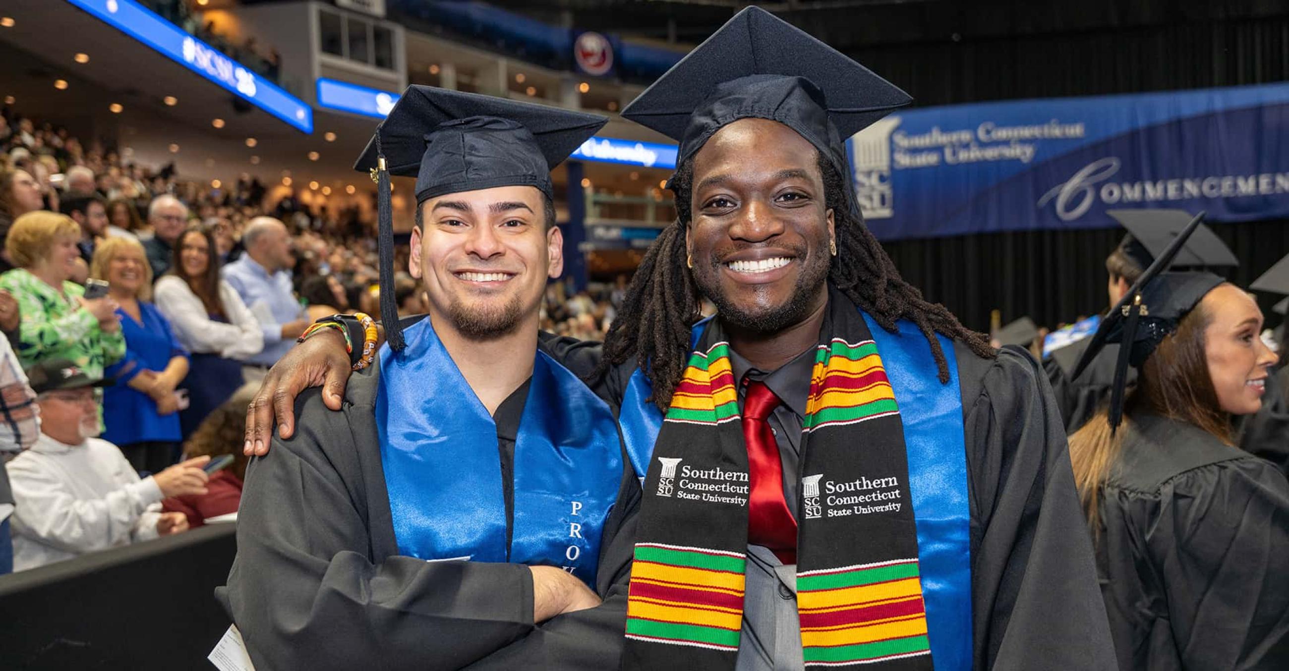 two young men in graduation caps and gowns smile at the camera