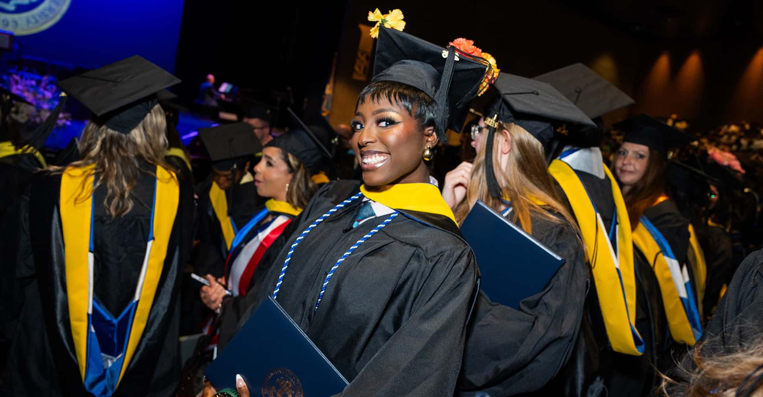 a young woman in graduation cap and gown smiles at the camera