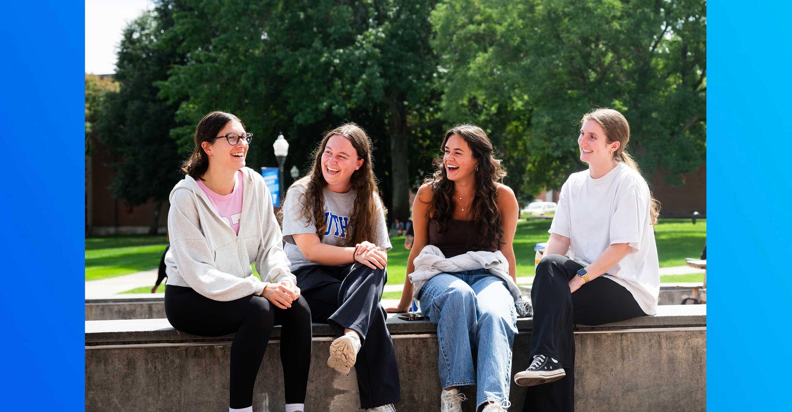 Four students at the campus quad laughing and chatting