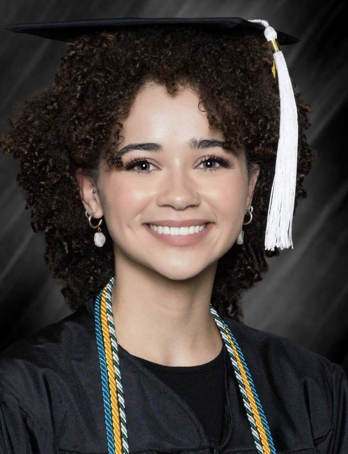 "Headshot of Jassmyne Lonski, twenty something lady with very curly brown hair wearing graduation regalia. 