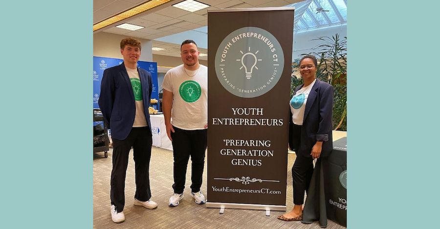 Three students standing next to a Youth Entrepreneurs sign